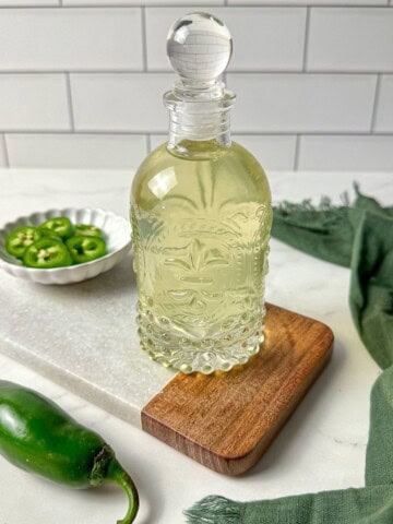 Jalapeno simple syrup in a glass jar with a bowl of sliced jalapenos.