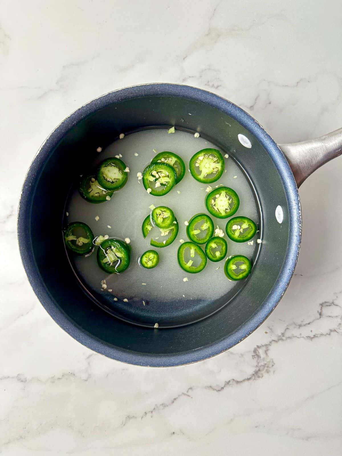 Sugar, water, and slices of jalapenos in a small saucepan.