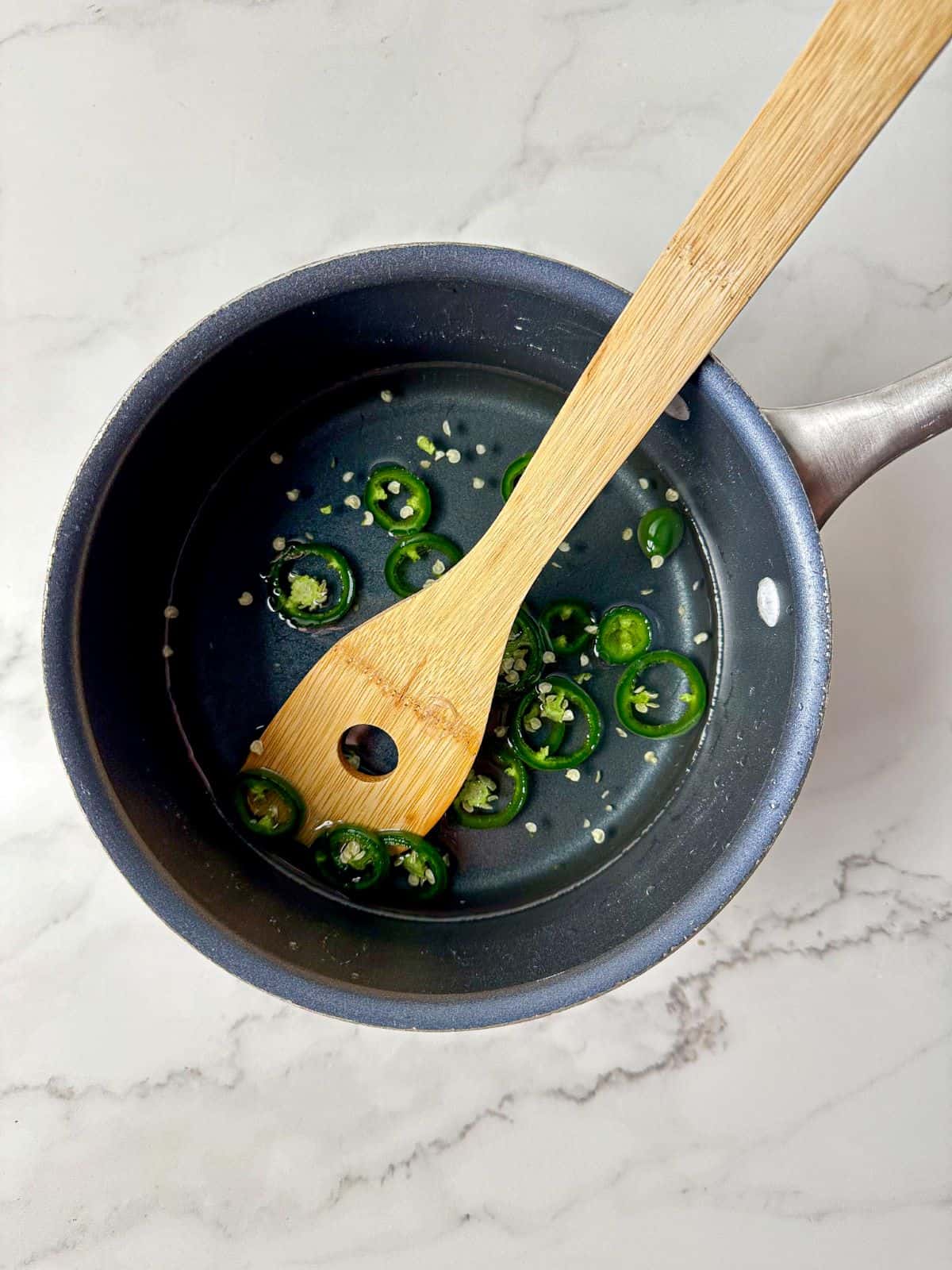 Jalapeno syrup in a saucepan with a wooden spoon.