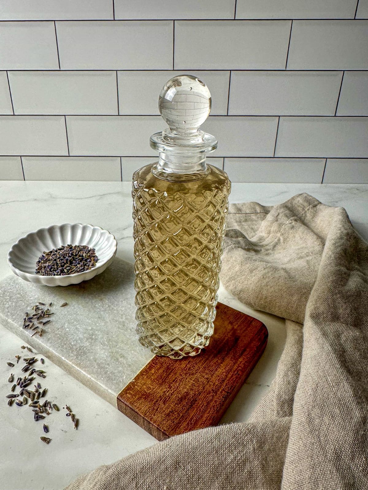 Lavender simple syrup in a glass jar surrounded by dried lavender and a kitchen towel.