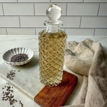 Lavender simple syrup in a glass jar surrounded by dried lavender and a kitchen towel.