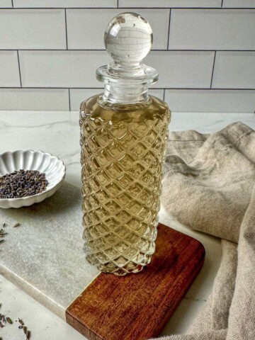 Lavender simple syrup in a glass jar surrounded by dried lavender and a kitchen towel.