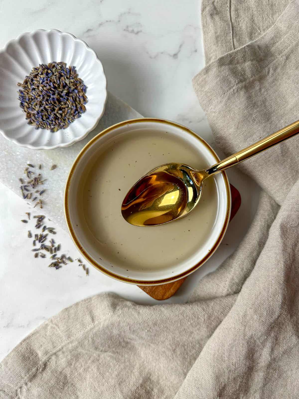 Homemade lavender simple syrup in a bowl with a spoon surrounded by dried lavender.