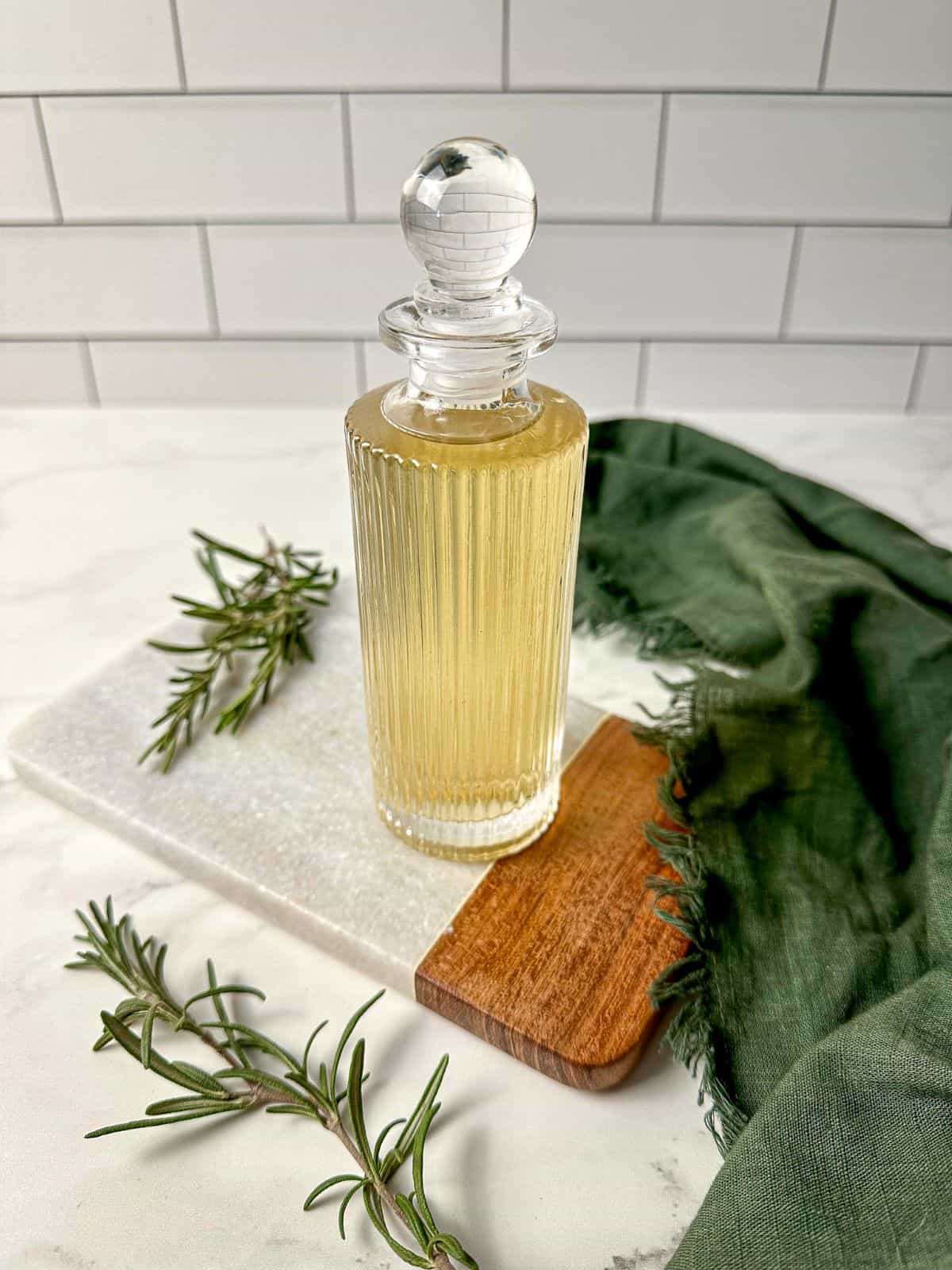 Rosemary simple syrup in a glass jar surrounded by fresh rosemary and a green kitchen towel.