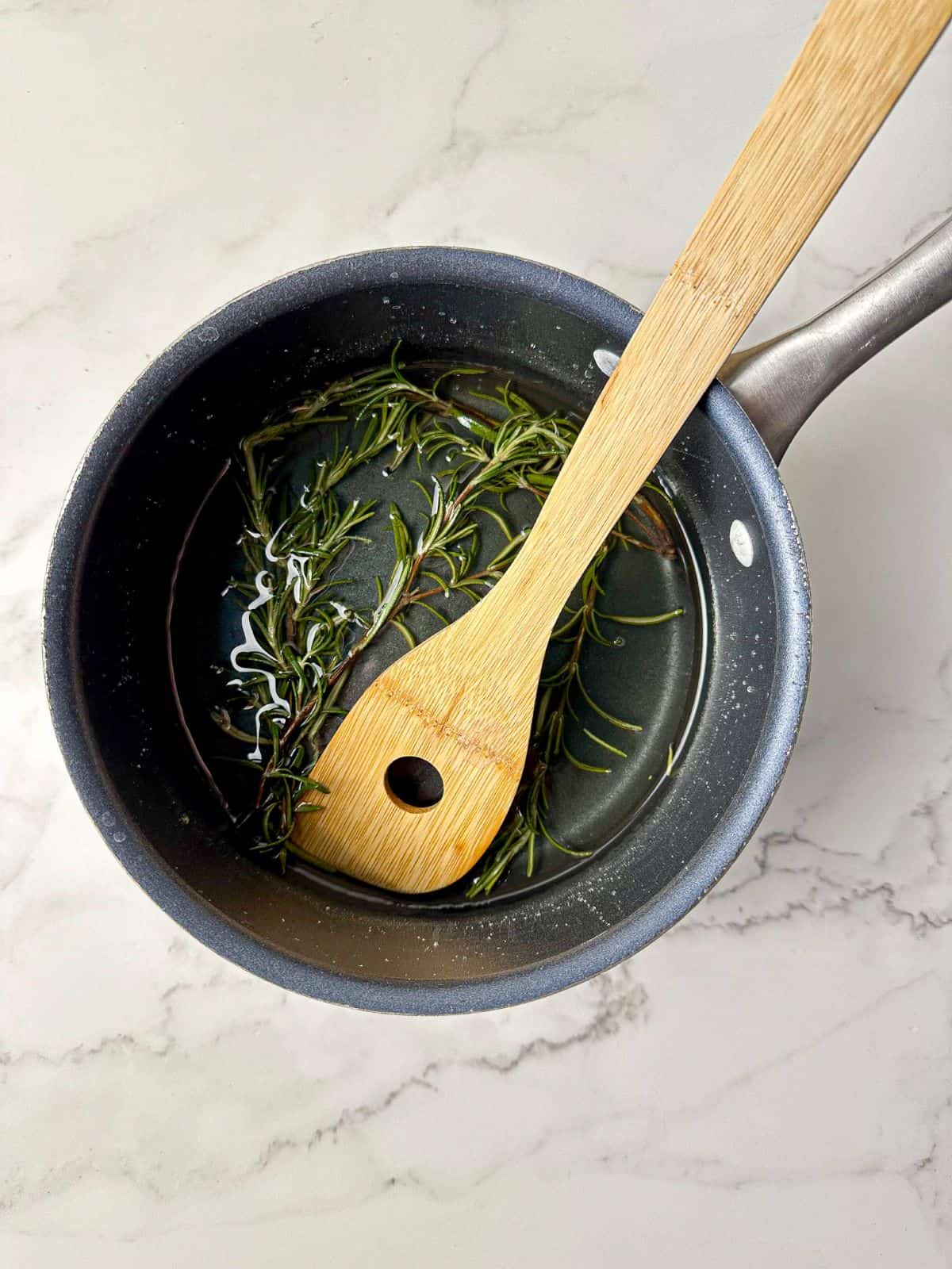 Rosemary syrup in a saucepan with a wooden spoon.