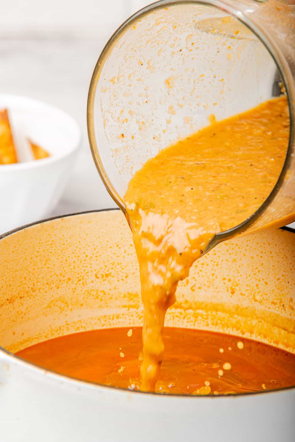 Pouring blended mixture into a large pot of tortilla soup.