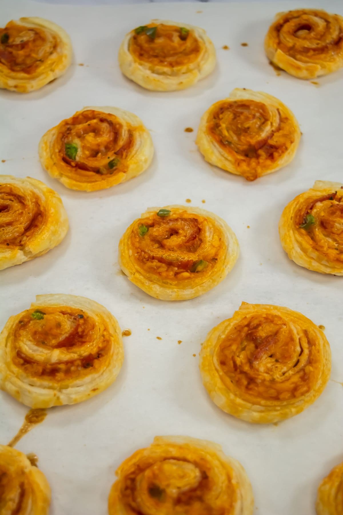 Baked pepperoni pinwheels on parchment paper.