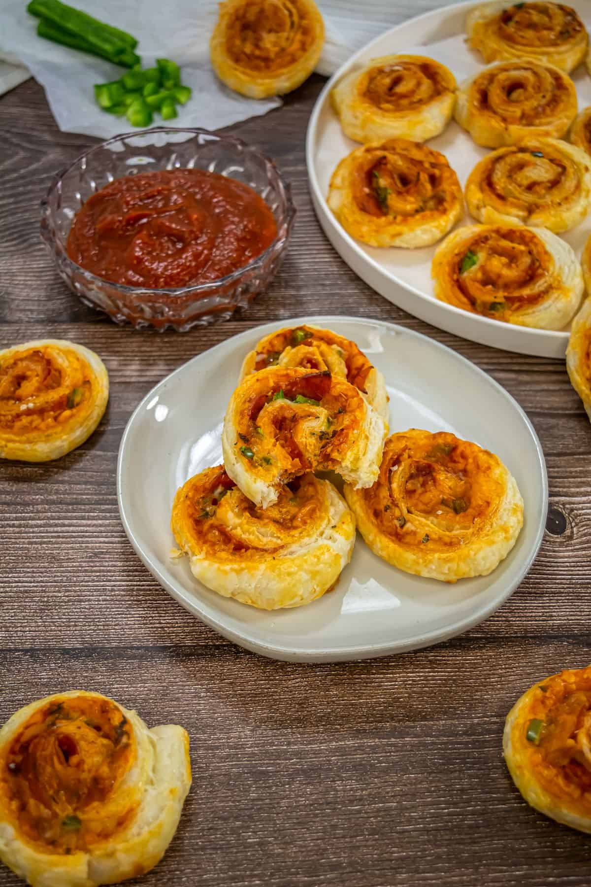 Puff pastry pizza pinwheels made with cheese and pepperoni on a platter with a bowl of marinara sauce.