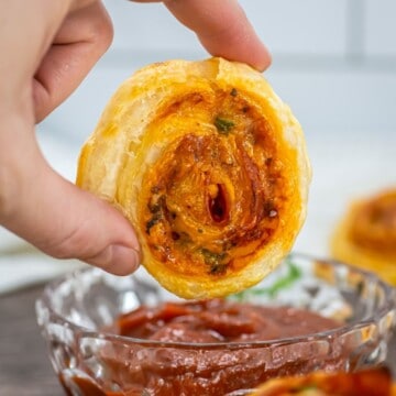 A hand dipping a pepperoni pizza pinwheel in marinara sauce.