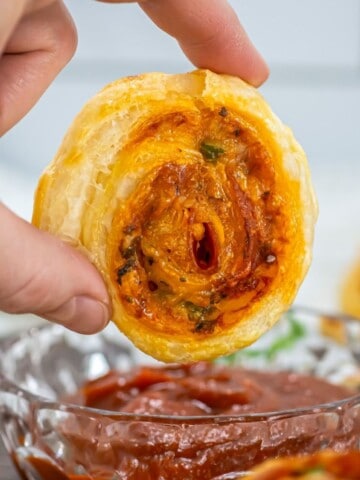 A hand dipping a pepperoni pizza pinwheel in marinara sauce.