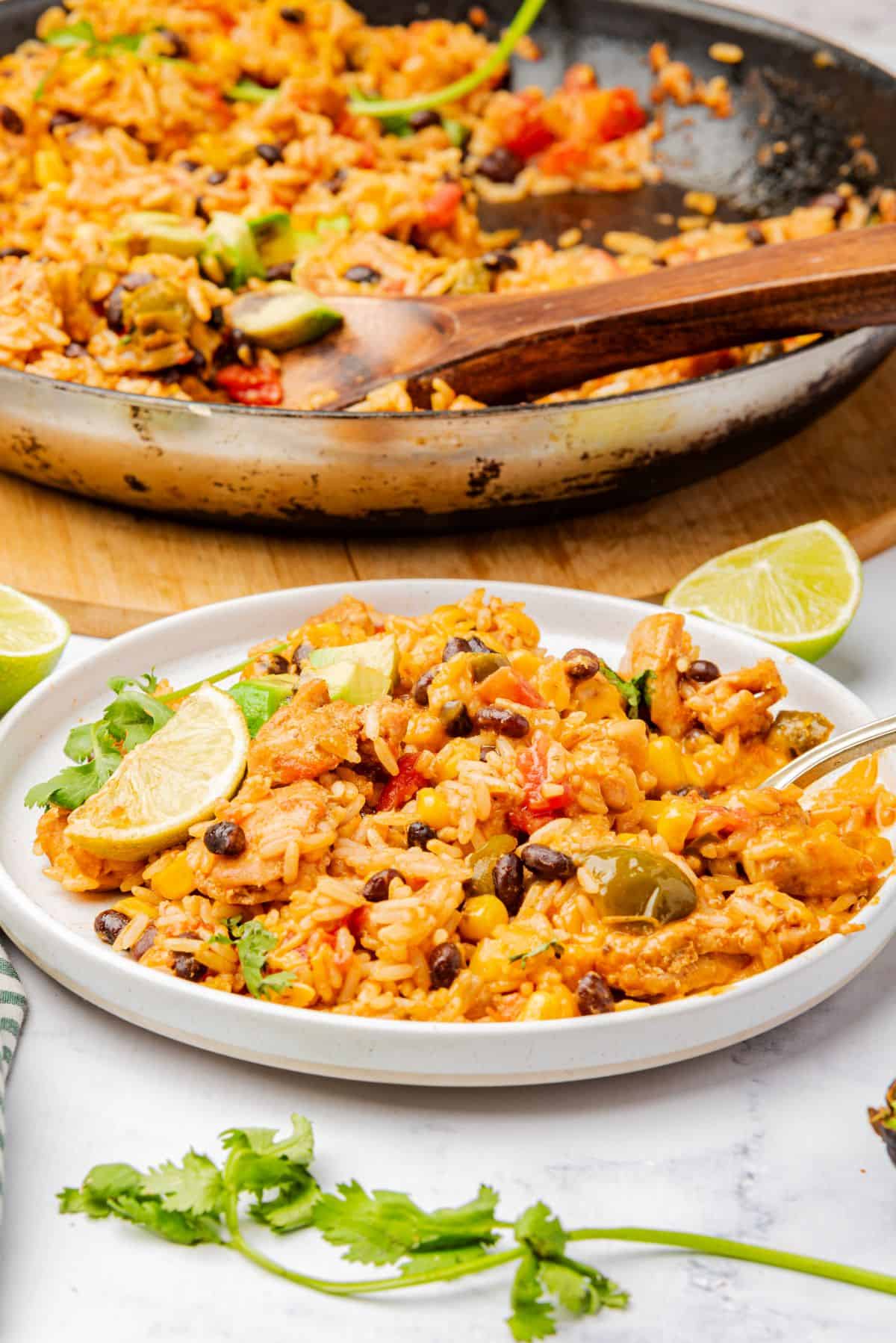 Cheesy Mexican chicken and rice on a plate with a spoon and lime wedge.