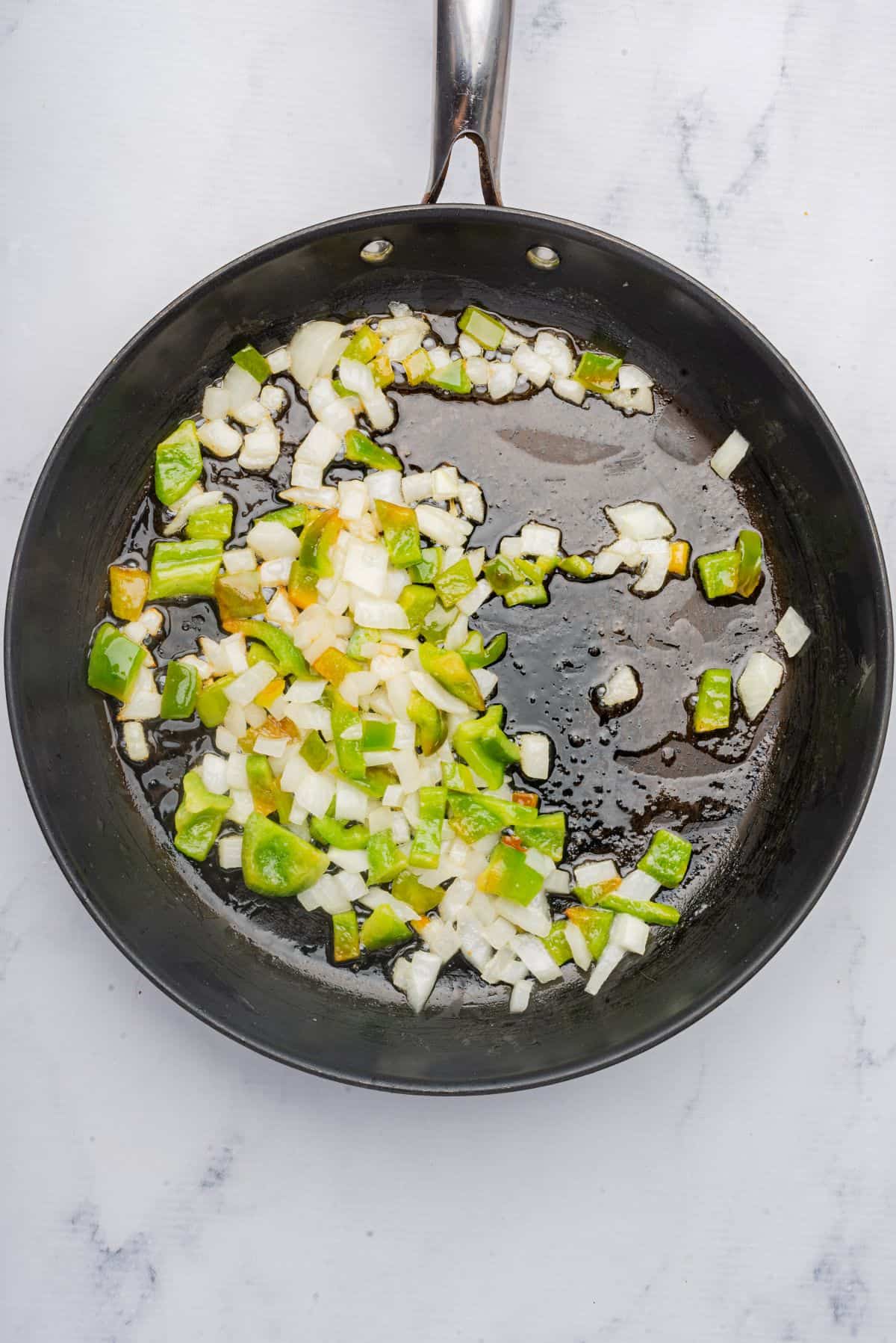 Onions and green bell peppers sauteing in a skillet.