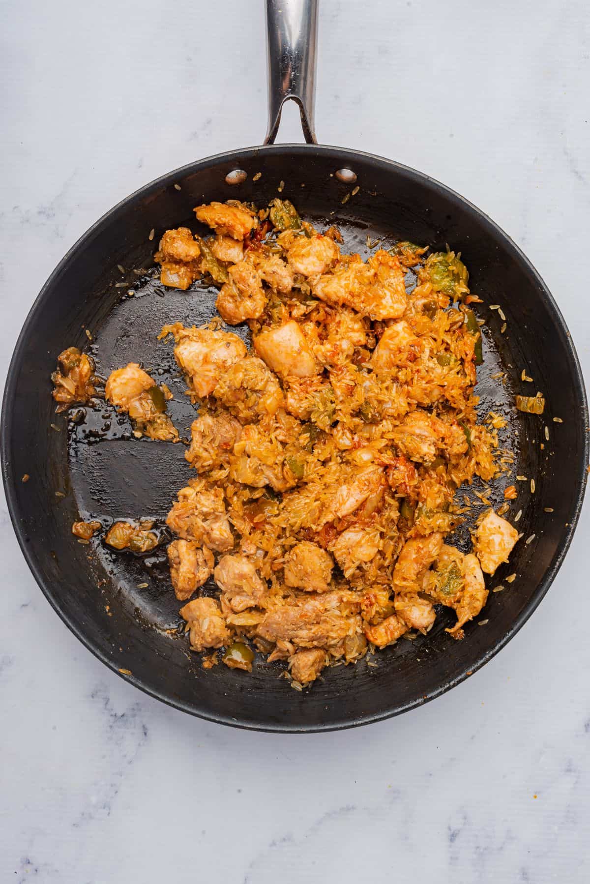 Rice and tomato paste added to chicken thighs cooking in the skillet.