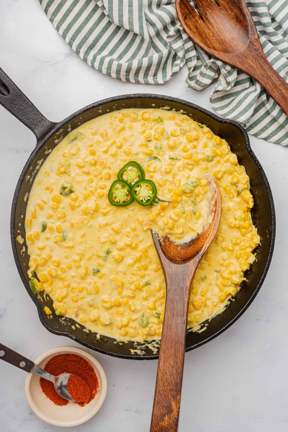 Jalapeno creamed corn in a skillet with a wooden spoon and topped with sliced jalapenos.