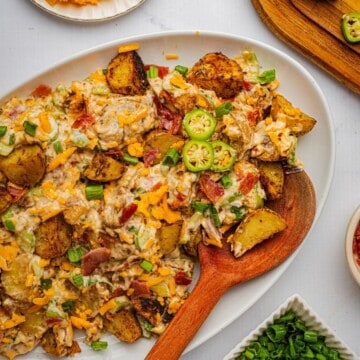 A creamy jalapeno popper potato salad on a platter with a wooden spoon.