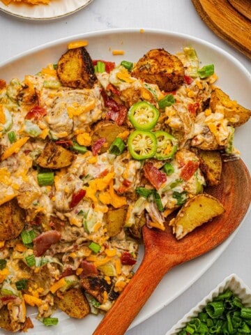 A creamy jalapeno popper potato salad on a platter with a wooden spoon.