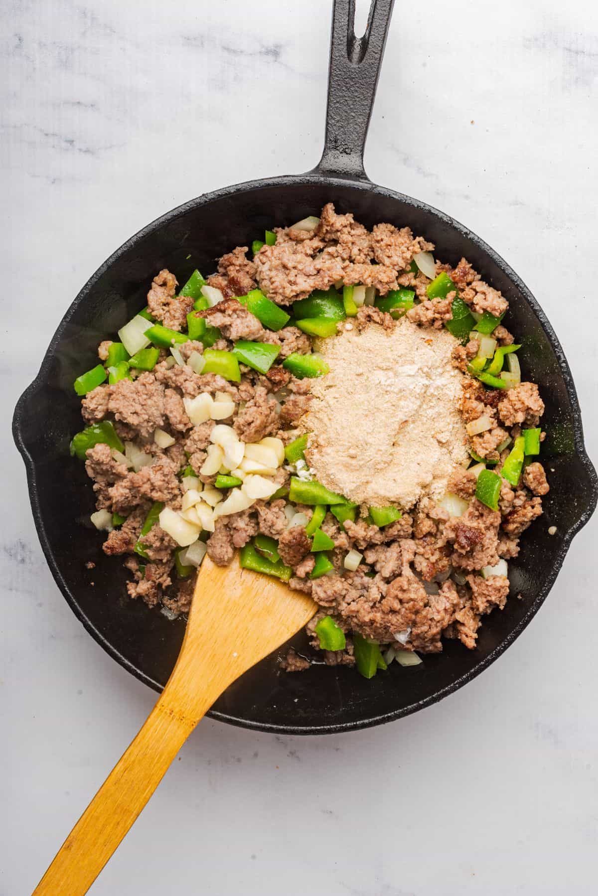 A cast iron skillet with ground beef, onions, and bell peppers.