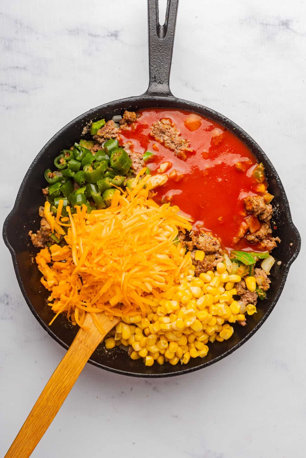 Skillet filled with ground beef, red enchilada sauce, corn, and cheese.