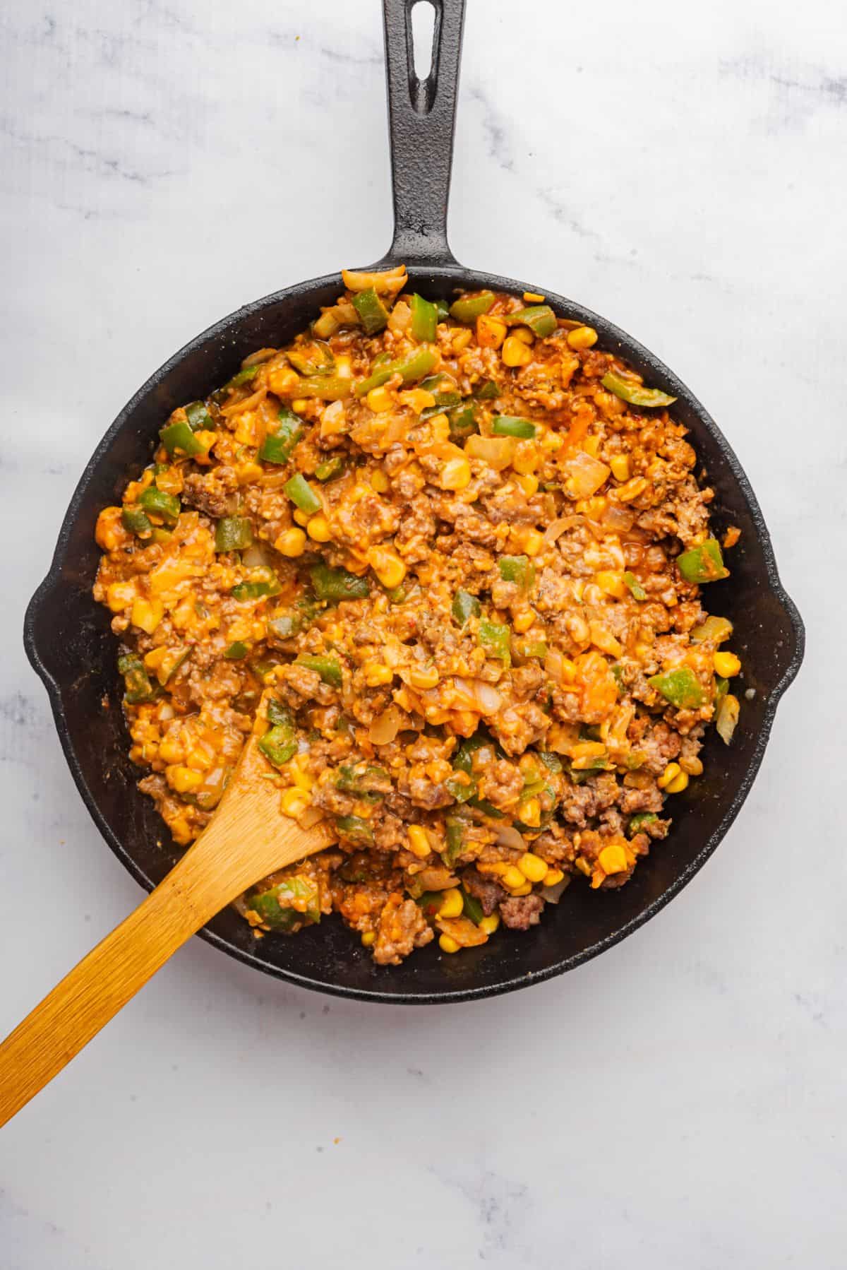 Ground beef meat mixture in a skillet with a wooden spoon.