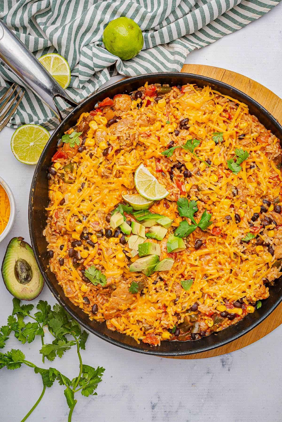 Cheesy Mexican chicken and rice in a skillet with diced avocado and lime wedge.