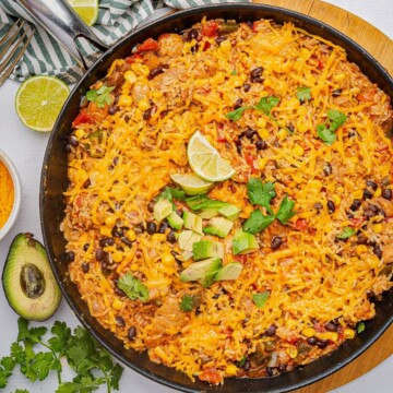 Cheesy Mexican chicken and rice in a skillet with diced avocado and lime wedge.