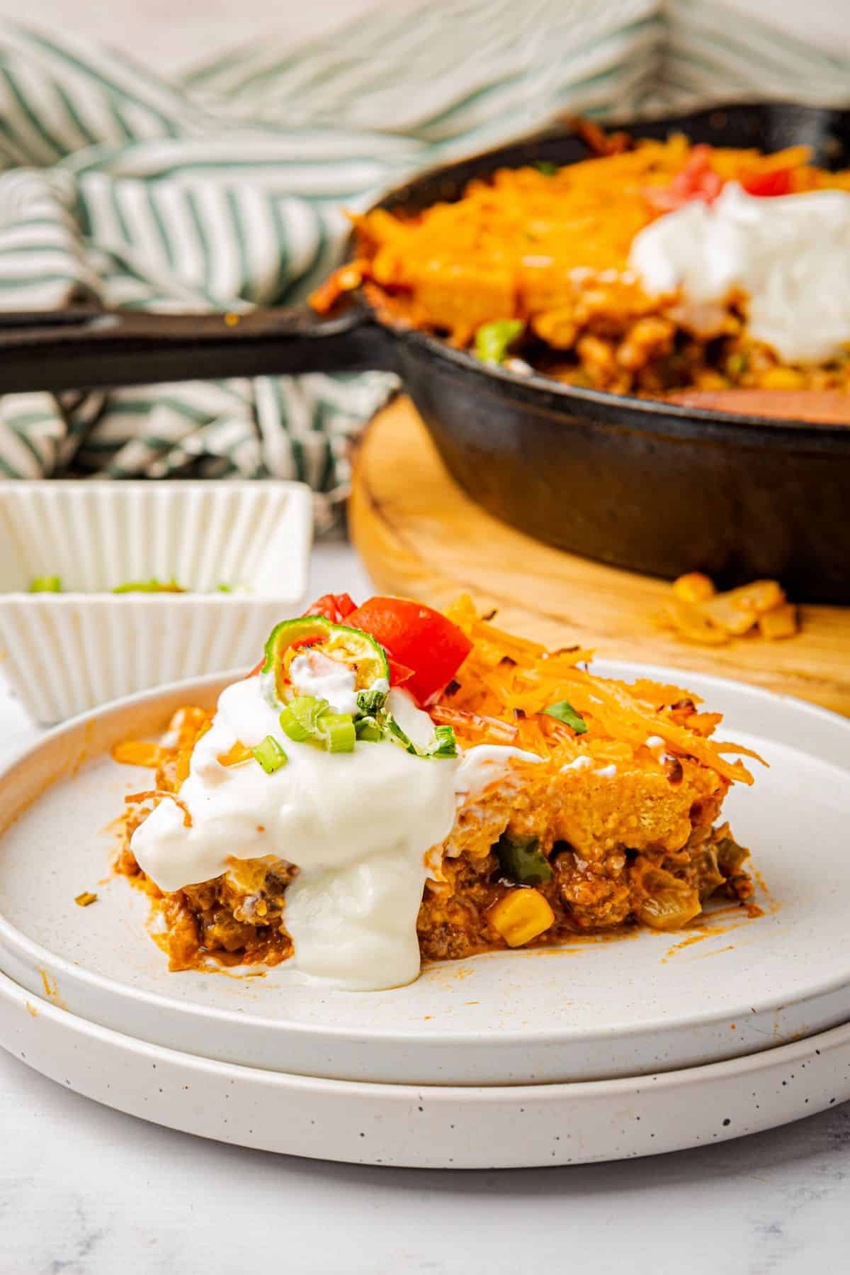 A slice of Jiffy tamale pie with cornbread crust topped with sour cream on a plate.