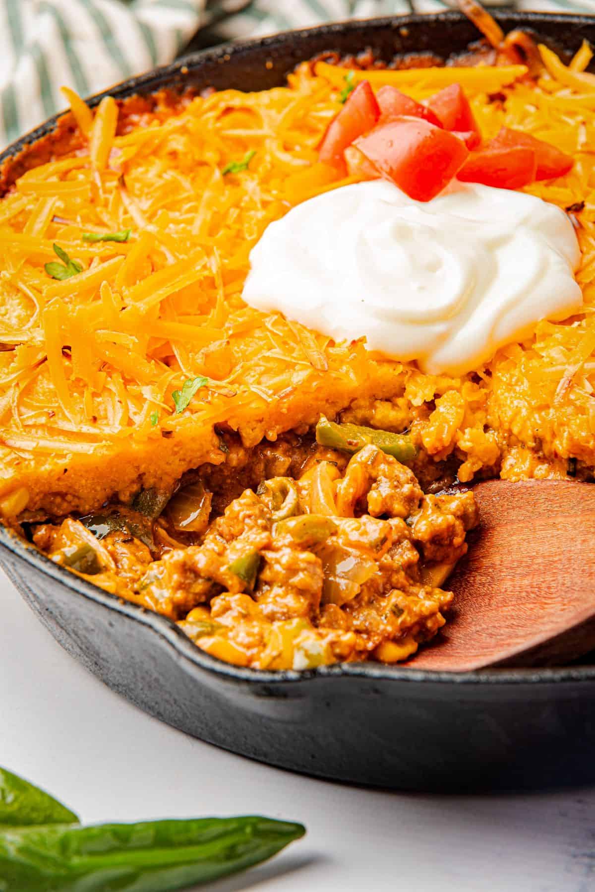 Jiffy tamale pie recipe in a skillet with a wooden spoon scooping out a serving.