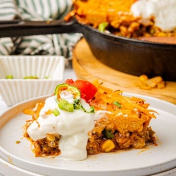 A slice of Jiffy tamale pie with cornbread crust topped with sour cream on a plate.