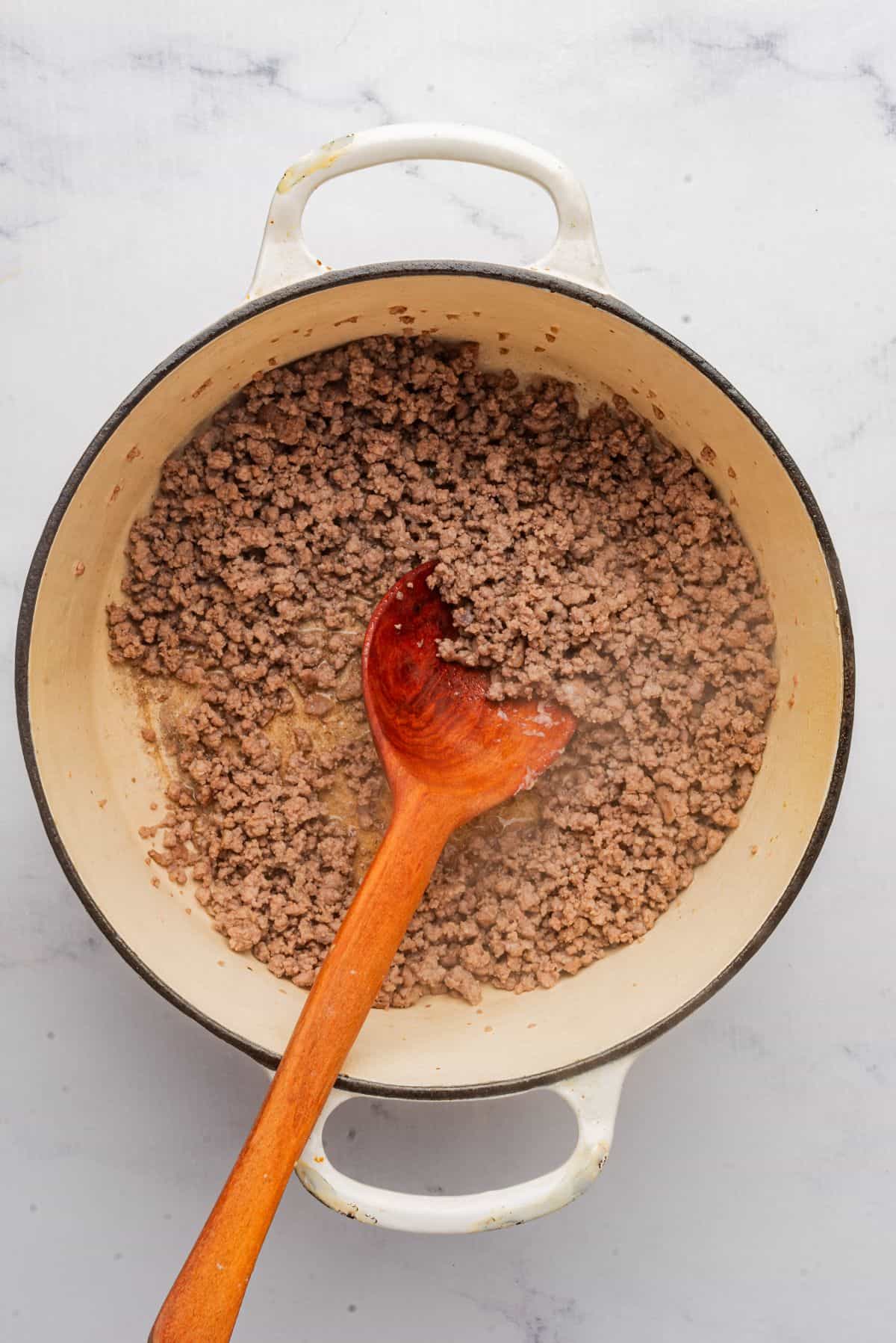 Browned ground beef in a large pot with a wooden spoon.