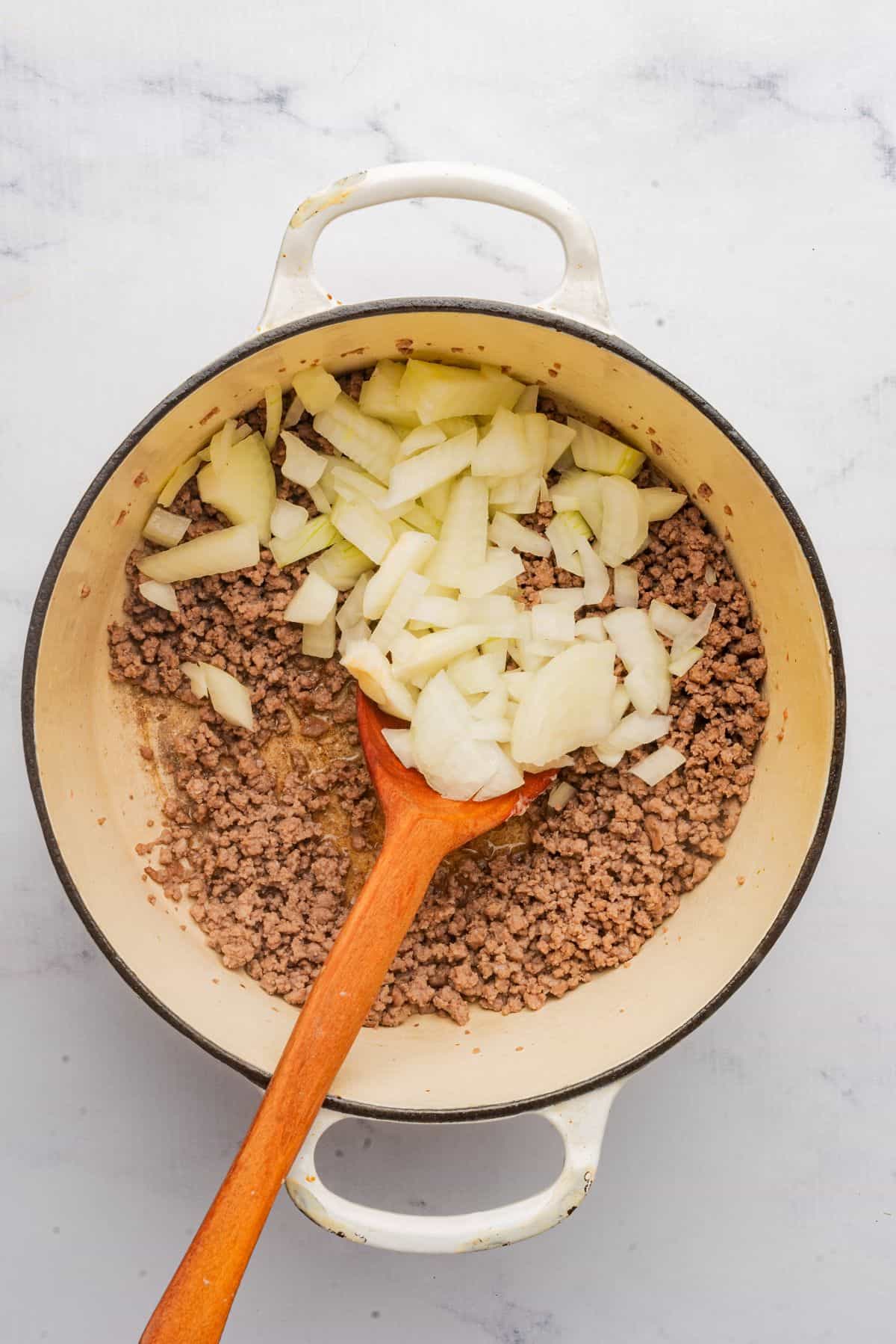 Chopped onions added to a large pot with ground beef.