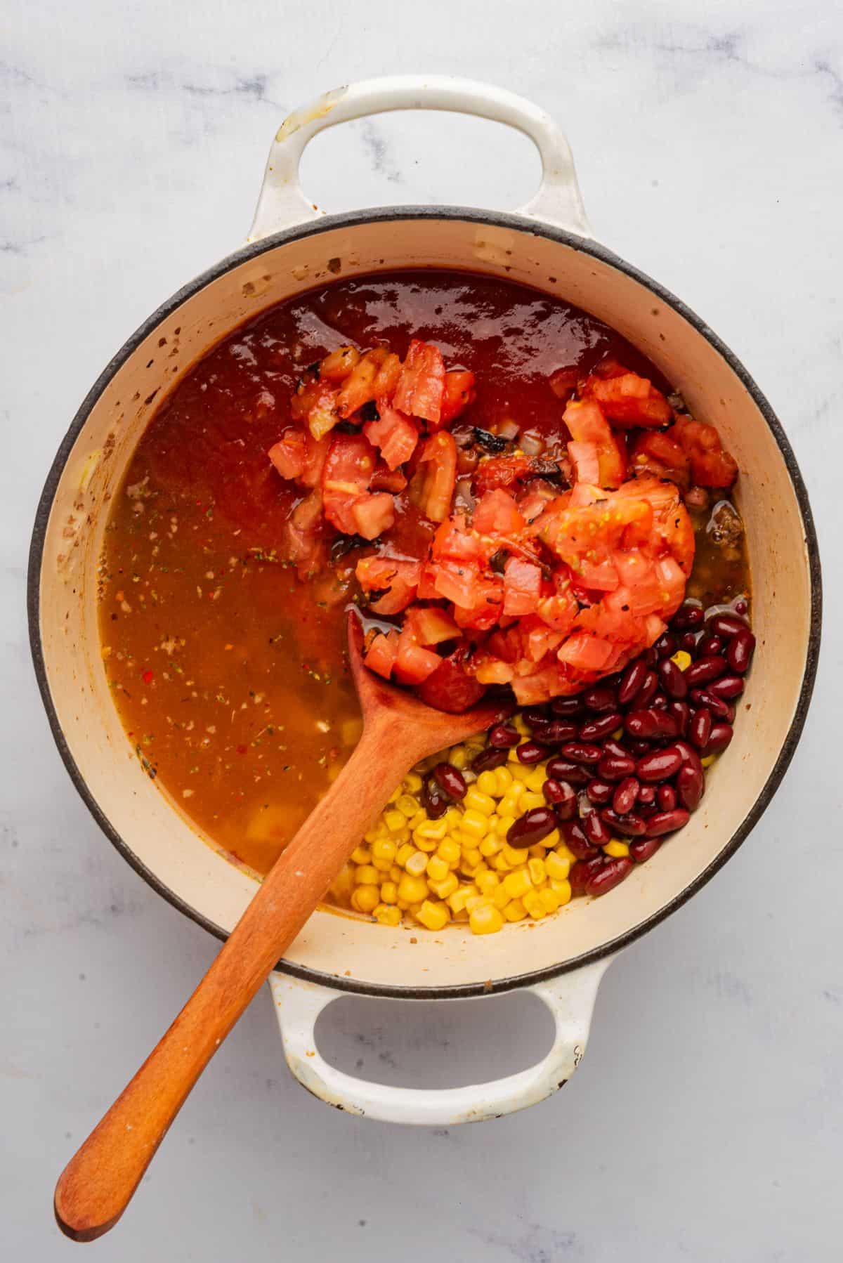 Beef enchilada soup cooking in a large pot with enchilada sauce, beef broth, diced tomatoes, corn, and beans.