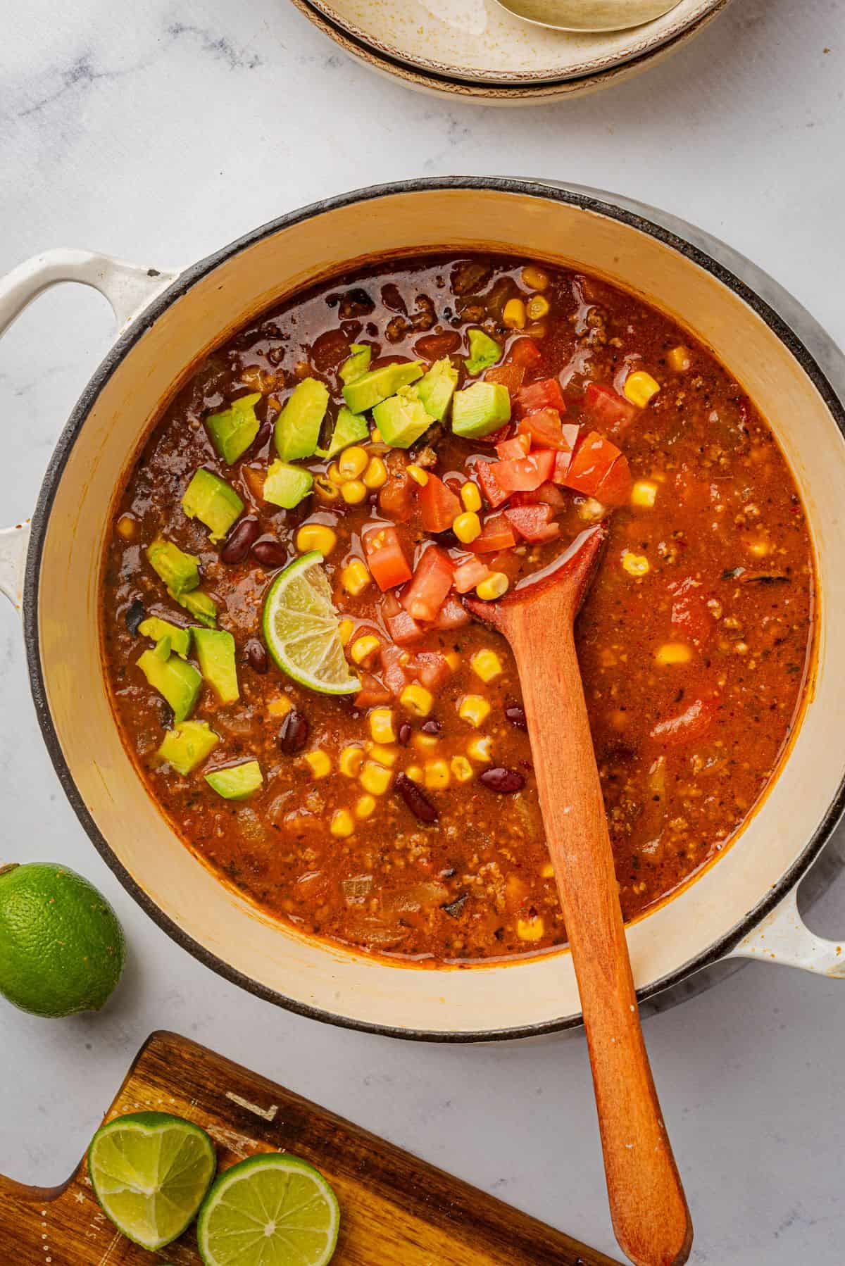 Homemade enchilada soup with ground beef in a pot with a wooden spoon.