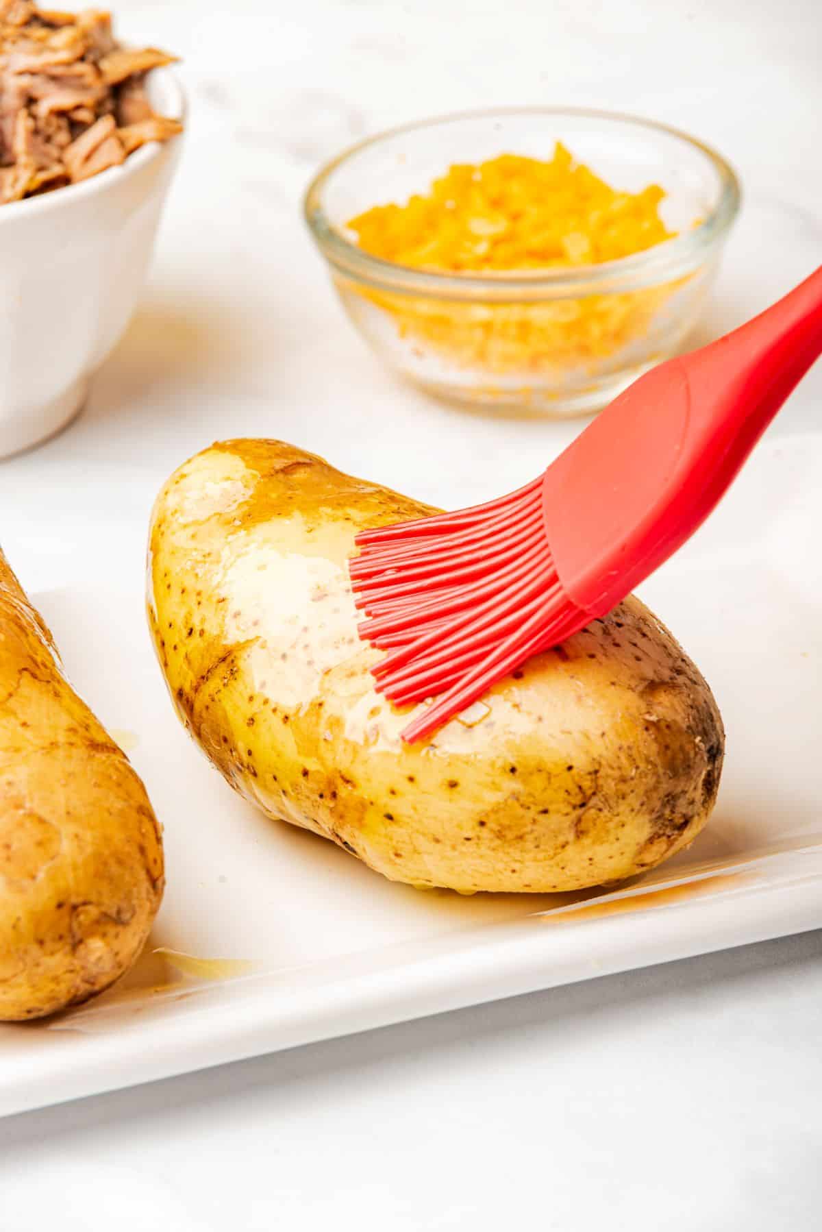 Brushing olive oil on a russet baking potato.