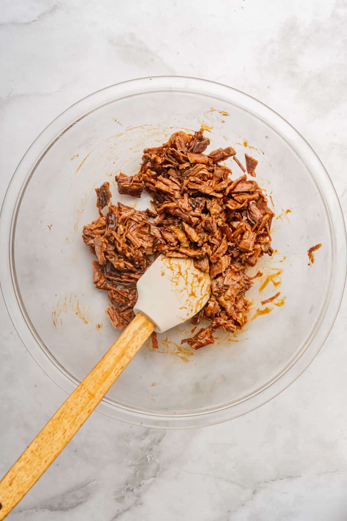 Chopped brisket in a bowl tossed in BBQ sauce with a spatula.