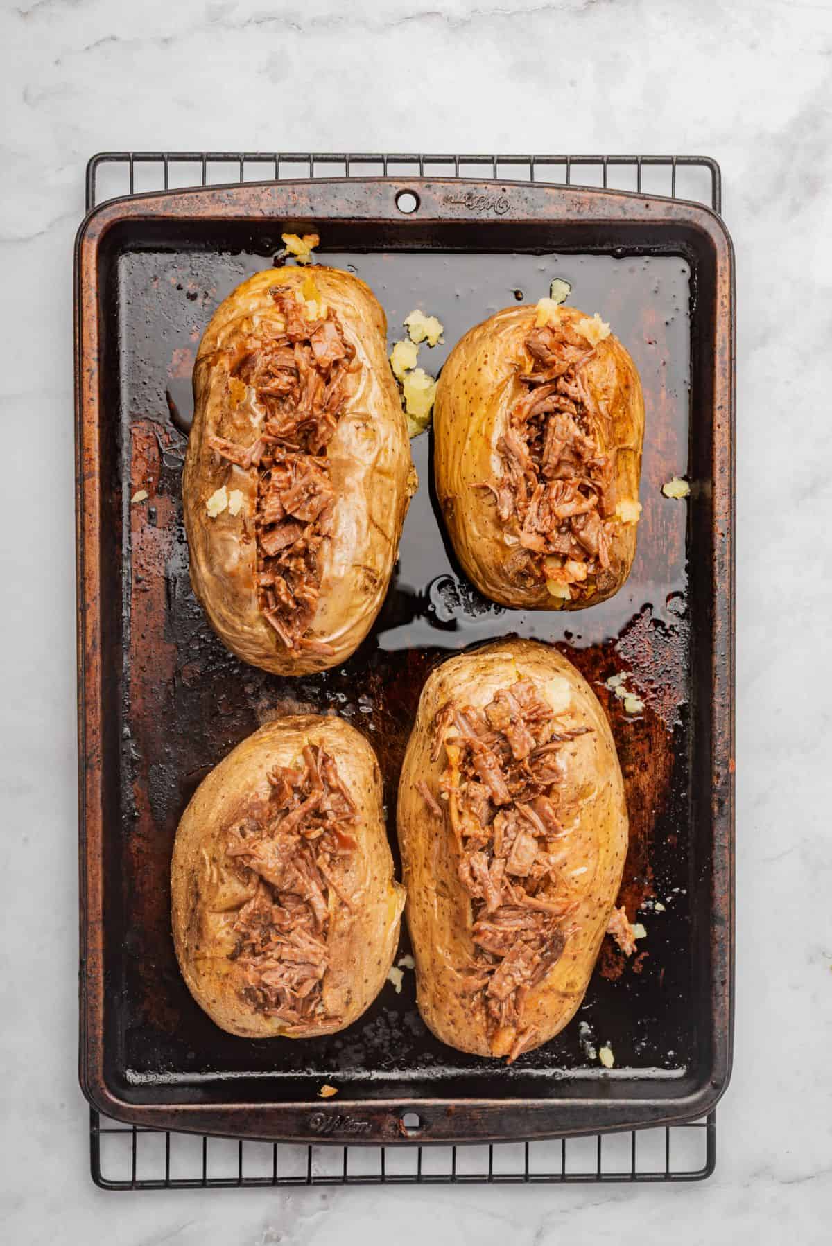 Four baked potatoes with brisket loaded into the center of each potato.