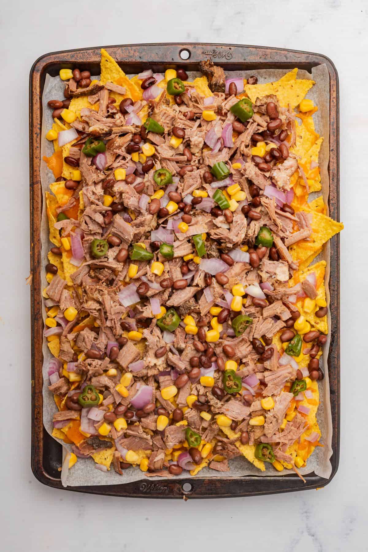 Nachos with shredded beef brisket and toppings on a sheet pan.