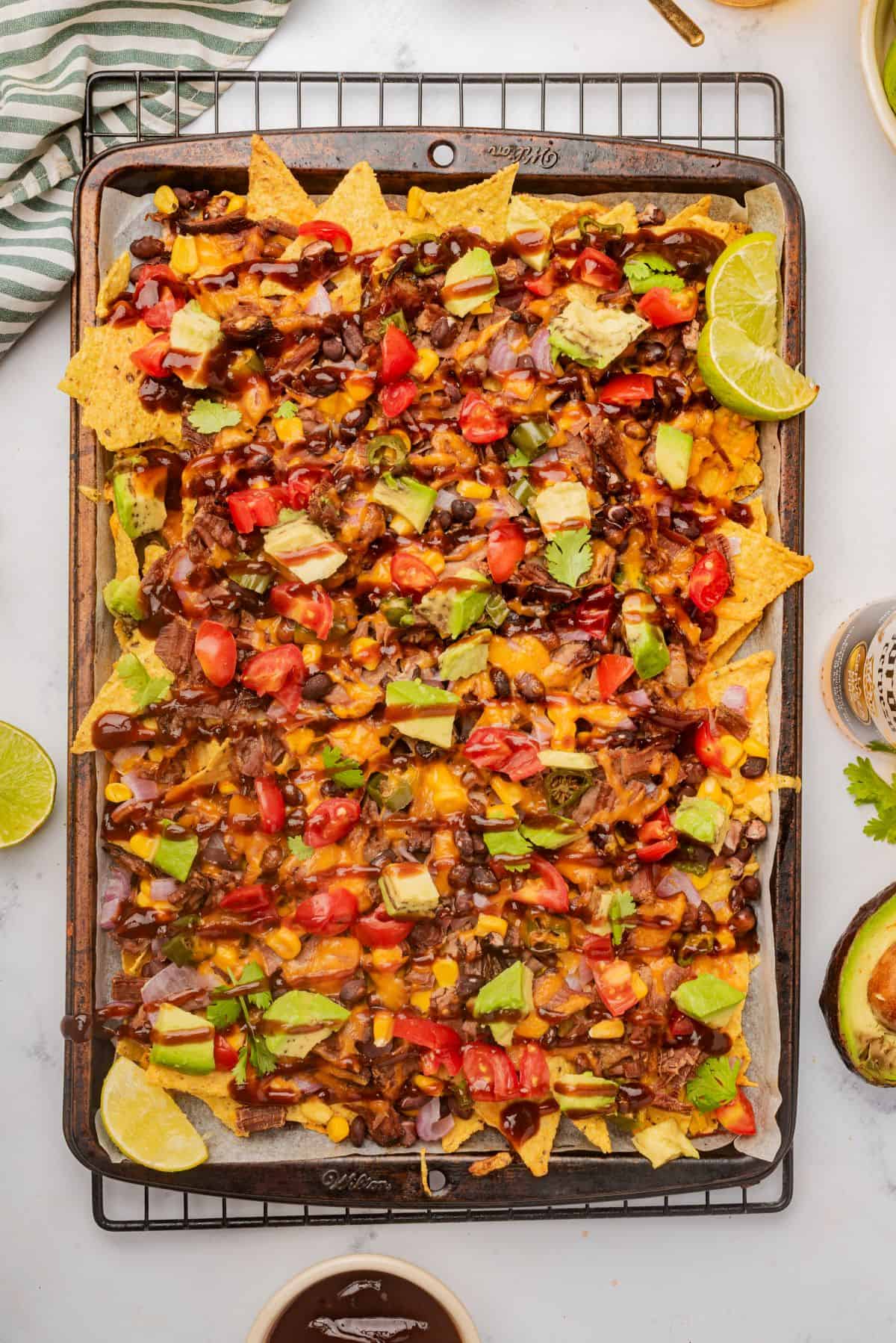 Loaded BBQ brisket nachos on a sheet pan with a drizzle of BBQ sauce over the toppings.