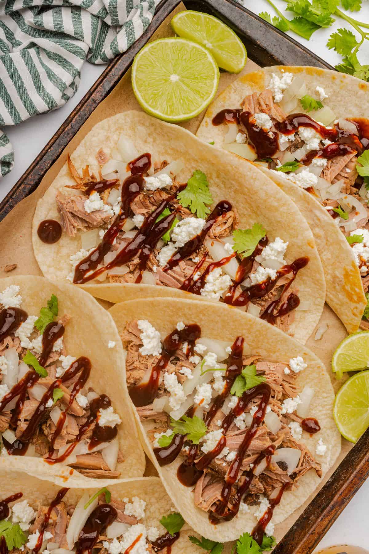 BBQ brisket tacos on a sheet pan with toppings of onions, cilantro, and cheese.