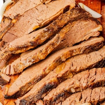 Thinly sliced braised beef brisket on a cutting board.