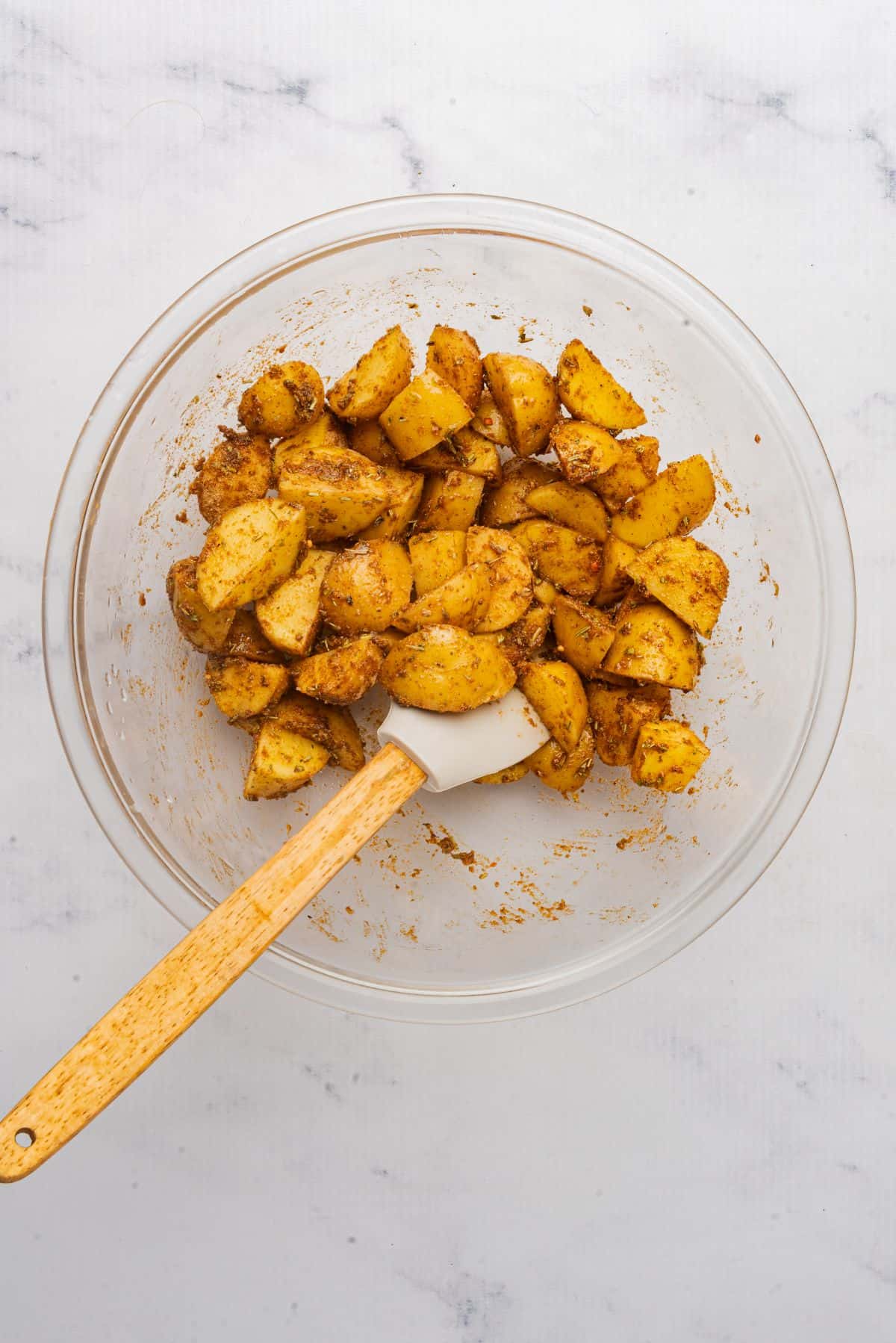 Yukon gold potatoes in a mixing bowl tossed in seasonings with a spatula.