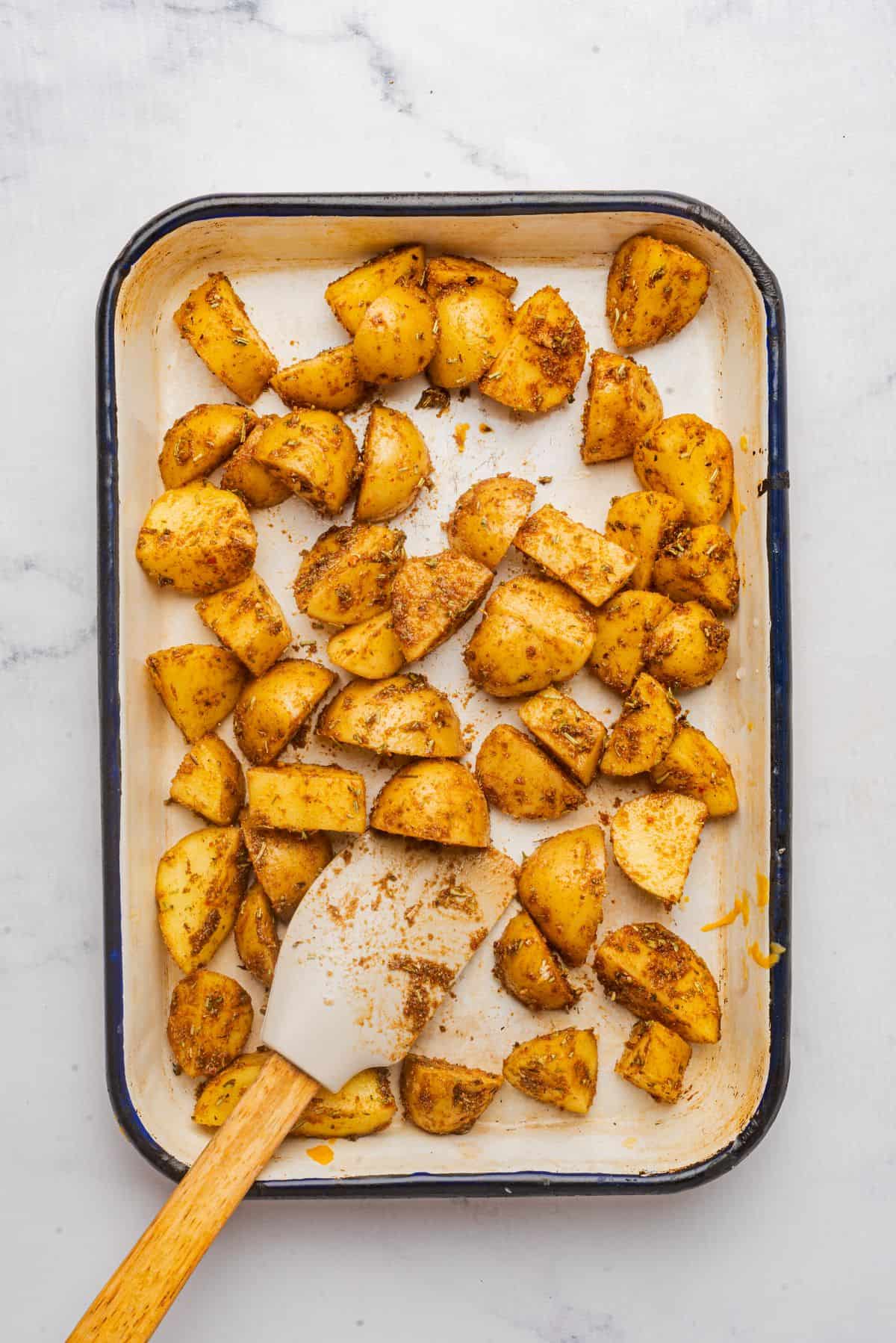 Quartered roasted potatoes in a baking dish with a spoon.