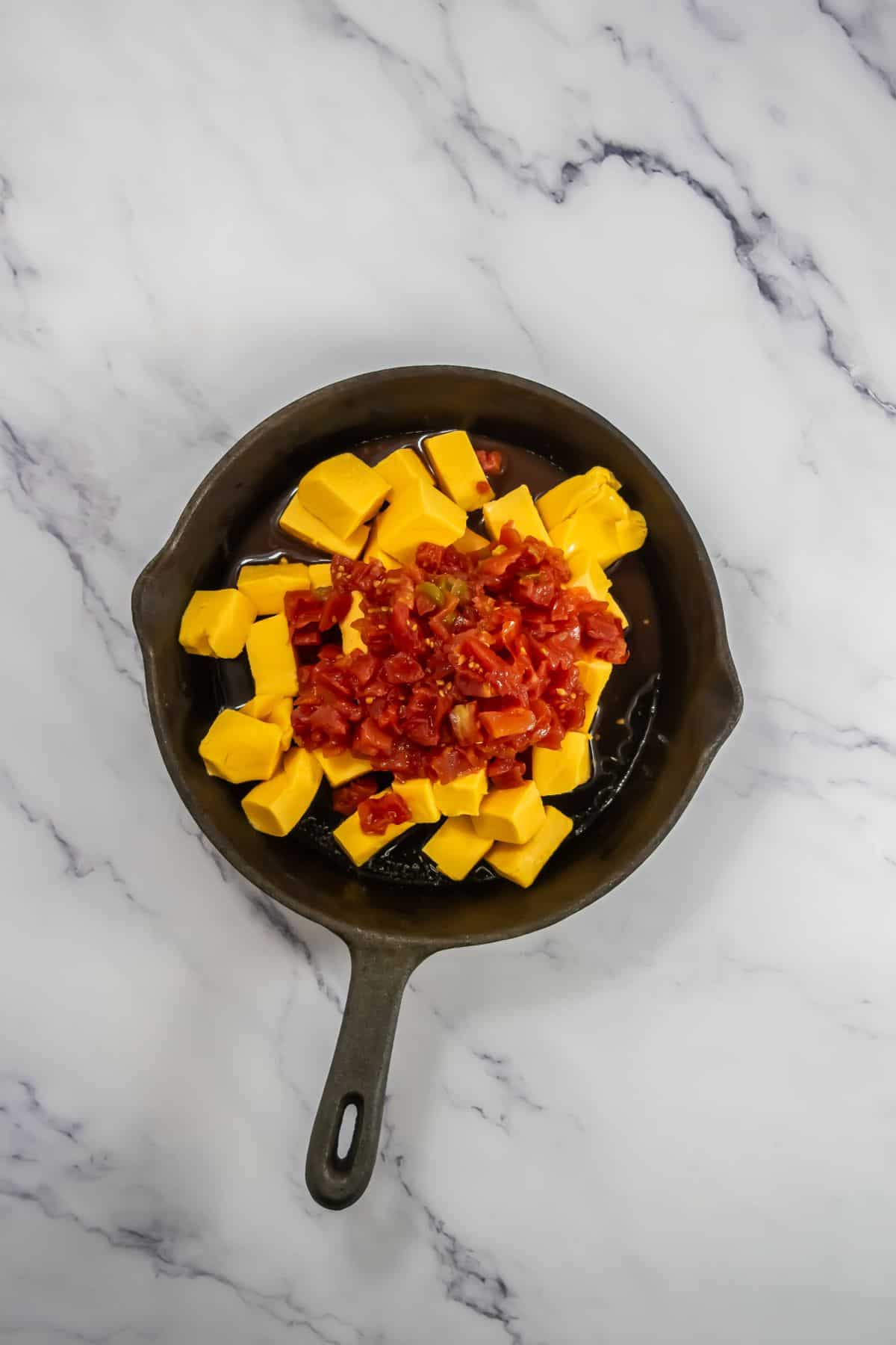 Velveeta cheese cubes and Rotel tomatoes with green chiles in a skillet.