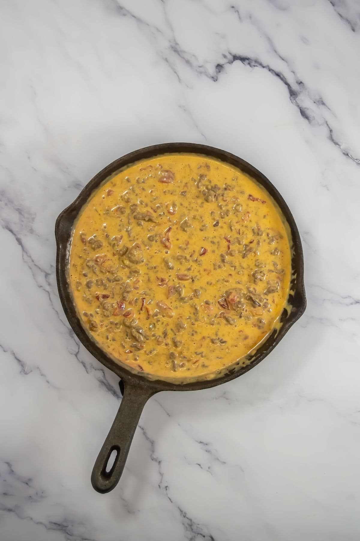 Melted Velveeta cheese, Rotel, and seasoned ground beef in a skillet.