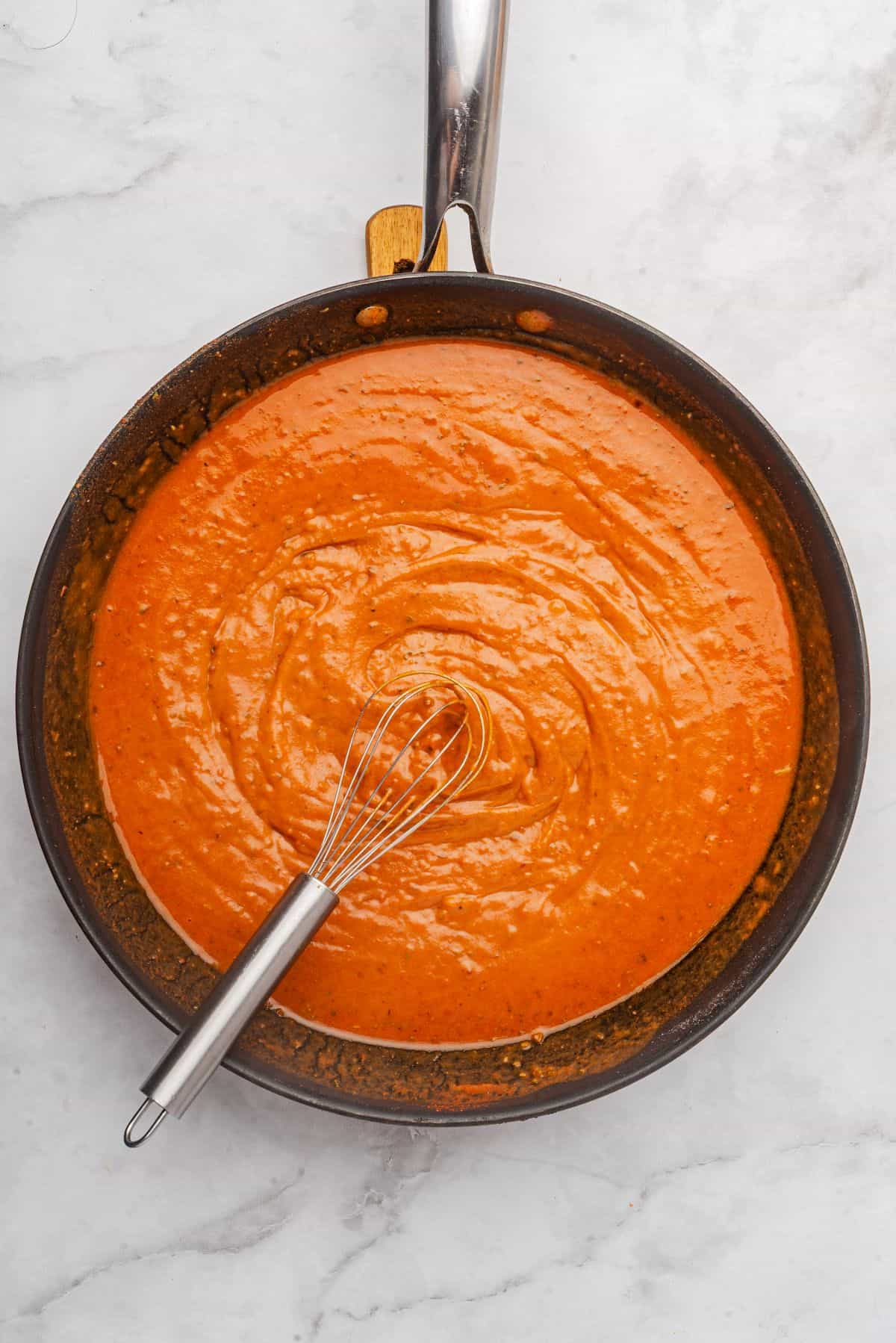 Red enchilada sauce recipe in a saucepan with a whisk.