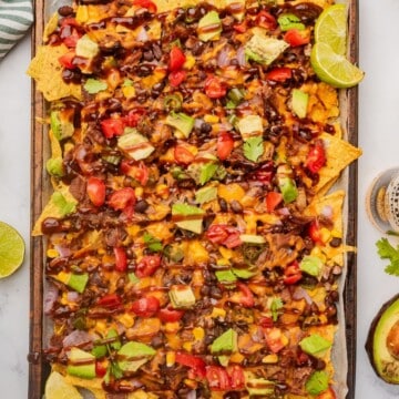 Loaded BBQ brisket nachos on a sheet pan with a drizzle of BBQ sauce over the toppings.