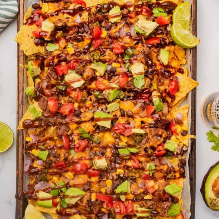 Loaded BBQ brisket nachos on a sheet pan with a drizzle of BBQ sauce over the toppings.