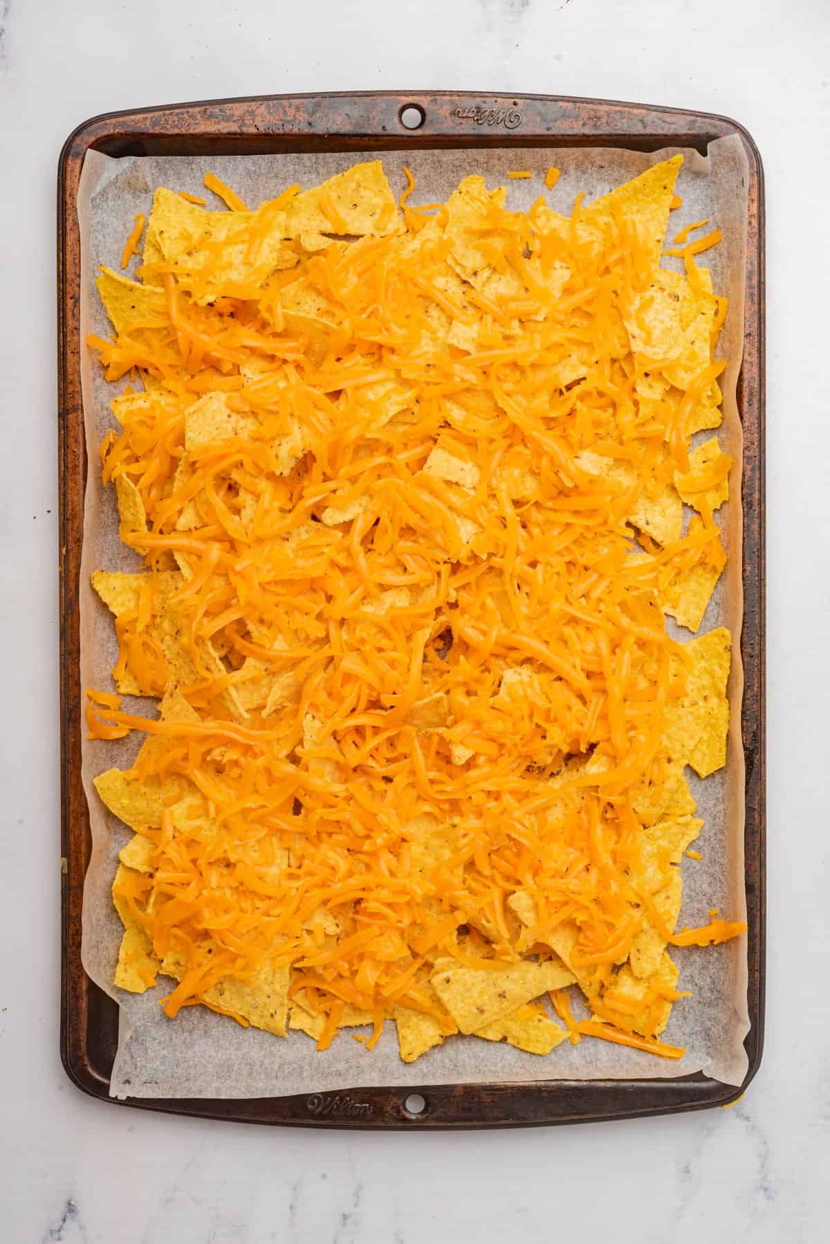 Tortilla chips and shredded cheese spread evenly on a sheet pan.