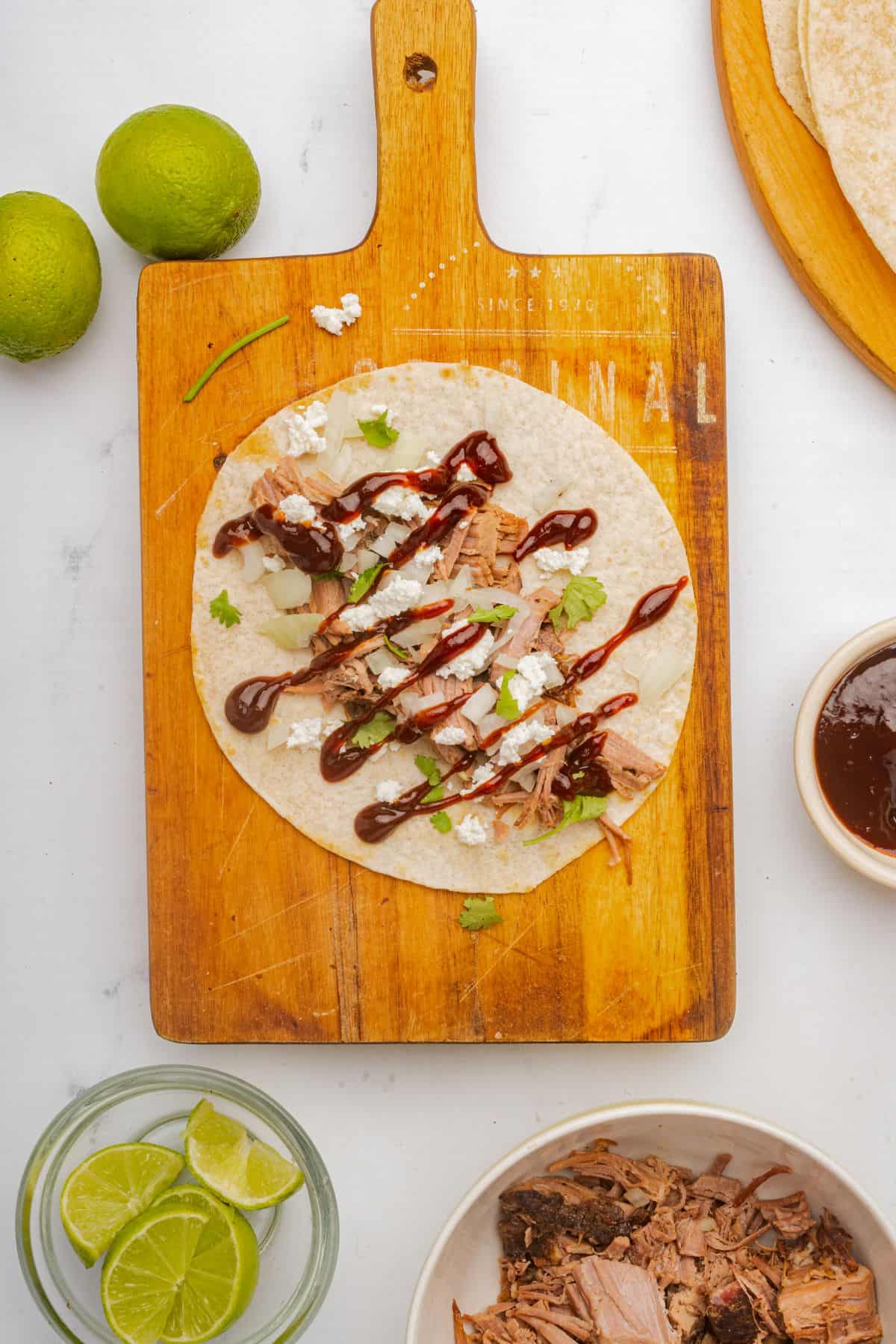 A brisket taco with BBQ sauce, onions, cheese, and cilantro assembled on a cutting board.