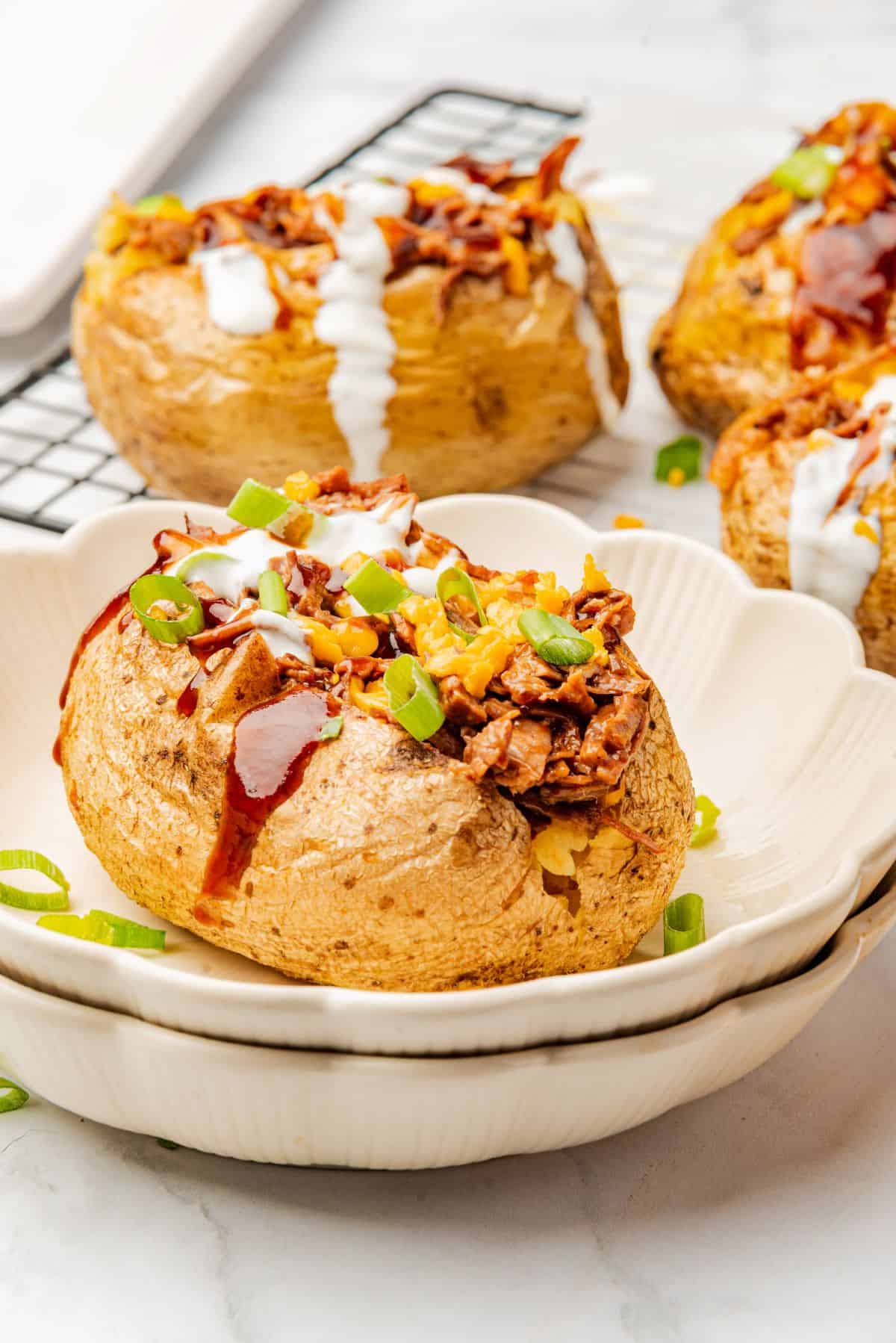 A loaded baked potato with brisket, BBQ sauce, cheese, and sour cream on a plate.