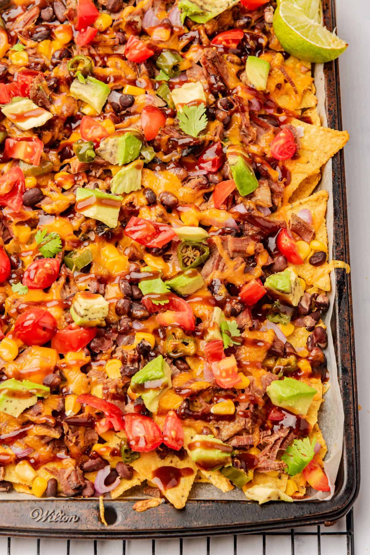 BBQ brisket nachos loaded with cheese, beans, corn, onions, tomatoes, avocado, and BBQ sauce.